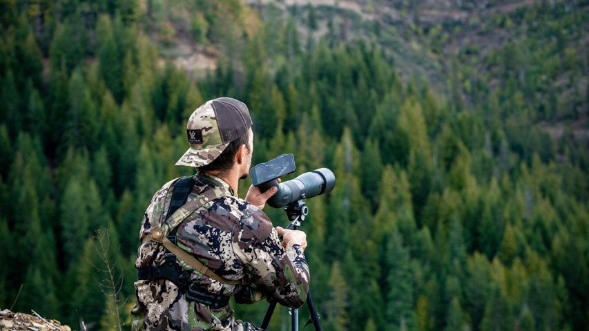 Hunter using spotting scope on mountain side.