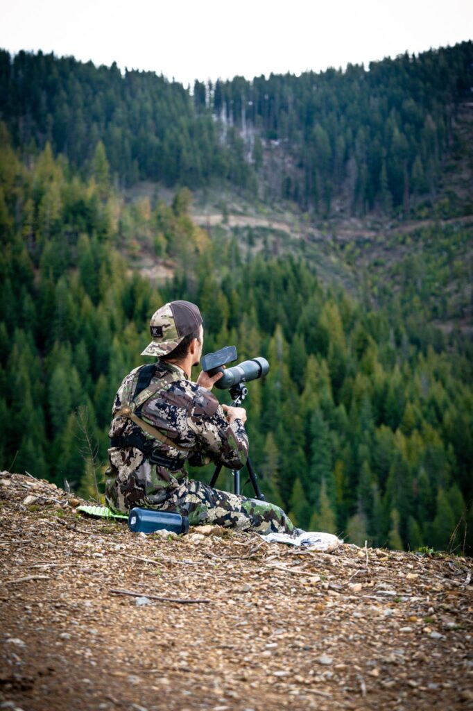 Hunter using spotting scope on mountain side.