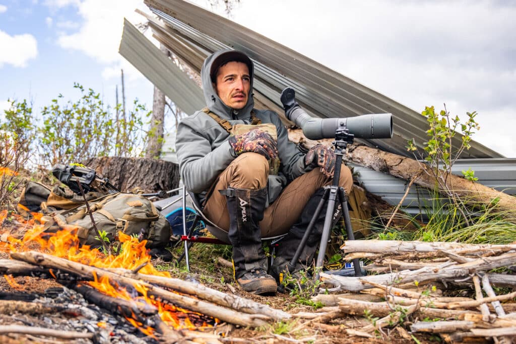 Elkshape Dan Staton glassing using a spotting scope in the backcountry under cover with a fire.