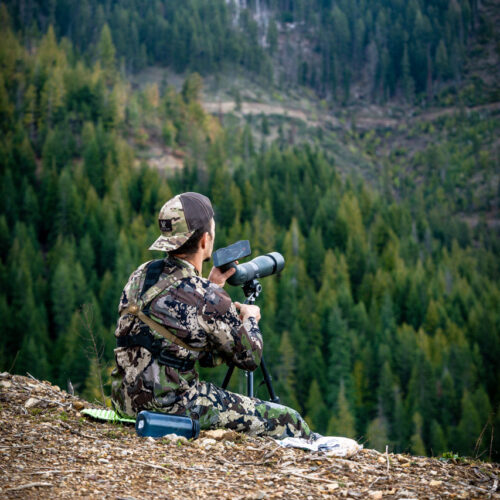 Hunter using spotting scope on mountain side.